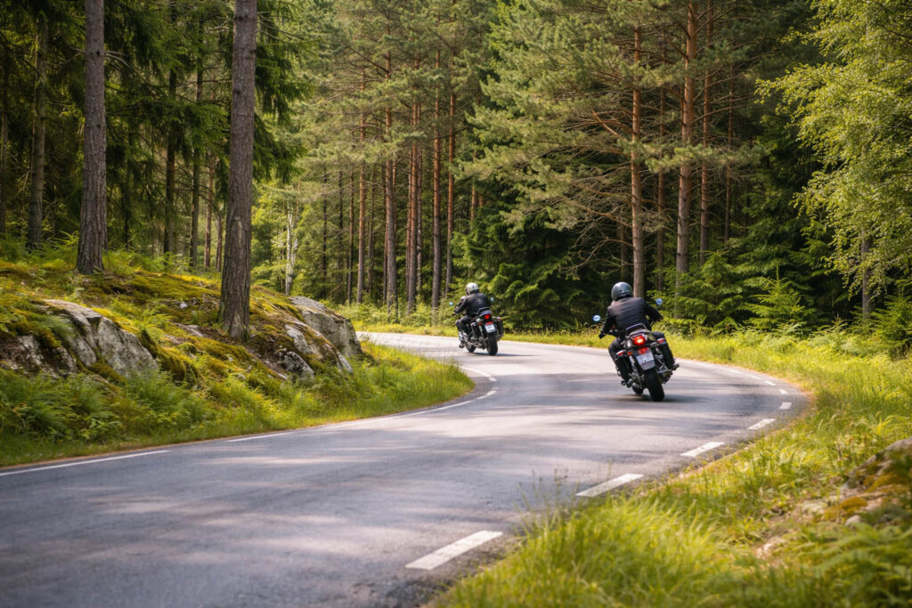 Två motorcyklar som åker på en landsväg i skogen.